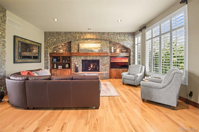 living room featuring built in features, a fireplace, and light hardwood / wood-style floors