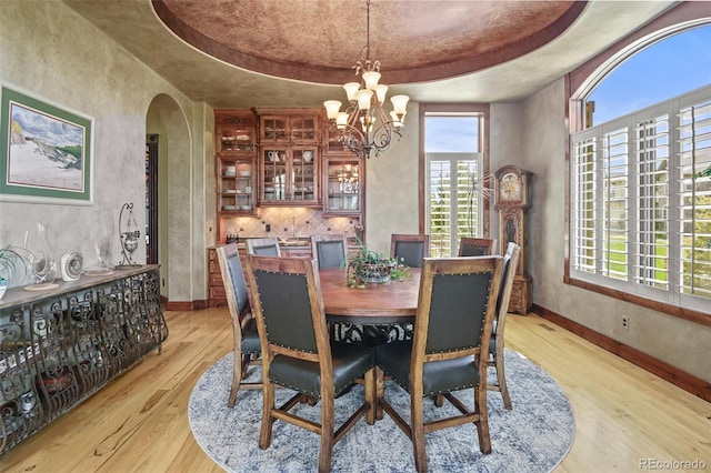 dining area featuring a notable chandelier, light wood-type flooring, and a tray ceiling