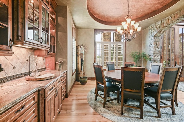 dining room featuring an inviting chandelier, light hardwood / wood-style floors, and a tray ceiling