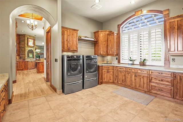 clothes washing area with light tile patterned flooring, cabinets, a chandelier, and washing machine and dryer