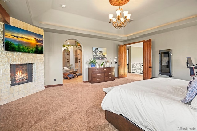 bedroom featuring an inviting chandelier, a tray ceiling, a stone fireplace, and light colored carpet