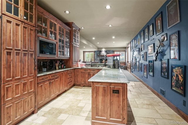 kitchen featuring black microwave, sink, a center island, light stone counters, and kitchen peninsula