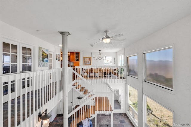 stairs with ornate columns, plenty of natural light, and ceiling fan with notable chandelier