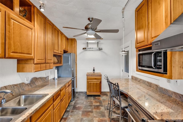 kitchen featuring ceiling fan, range hood, sink, stainless steel appliances, and a textured ceiling