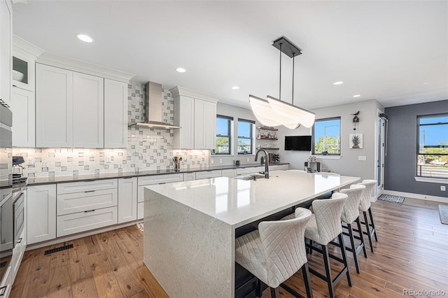 941 Saint Andrews Ln, Louisville, CO 80027 - kitchen featuring wall chimney range hood, backsplash, light wood-type flooring, a breakfast bar area, and recessed lighting