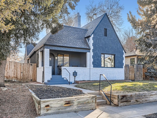 view of front of property with covered porch, brick siding, a chimney, and fence