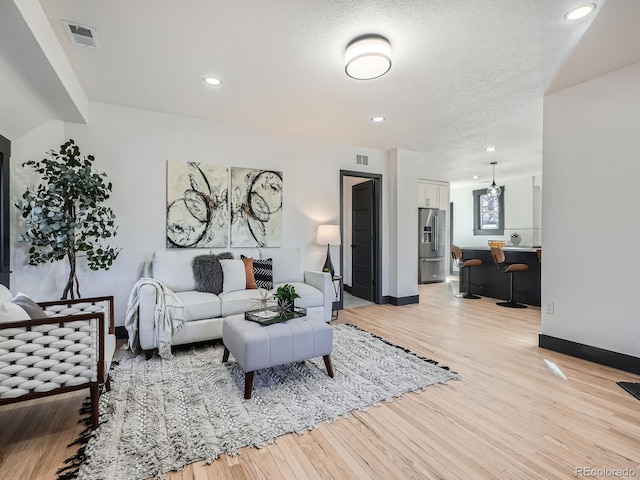 living area with a textured ceiling, light wood-style flooring, and visible vents