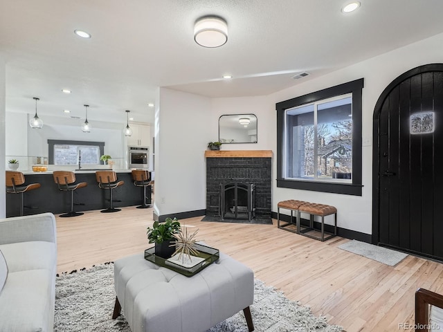 living area with light wood finished floors, a fireplace, visible vents, and baseboards