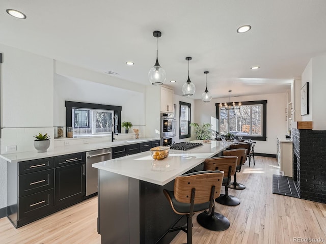 kitchen featuring dark cabinets, stainless steel appliances, a breakfast bar, light countertops, and pendant lighting