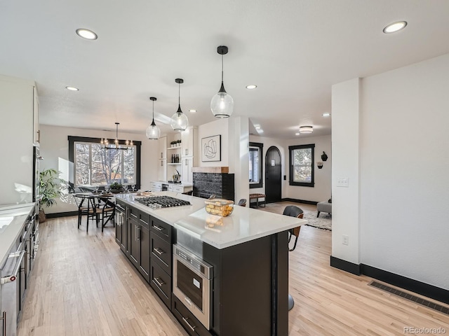 kitchen featuring decorative light fixtures, stainless steel appliances, light countertops, a kitchen island, and dark cabinets