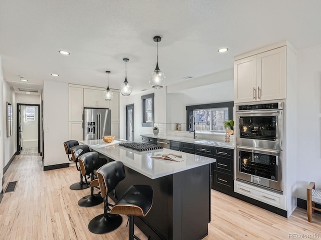 kitchen featuring visible vents, white cabinets, a kitchen island, appliances with stainless steel finishes, and pendant lighting