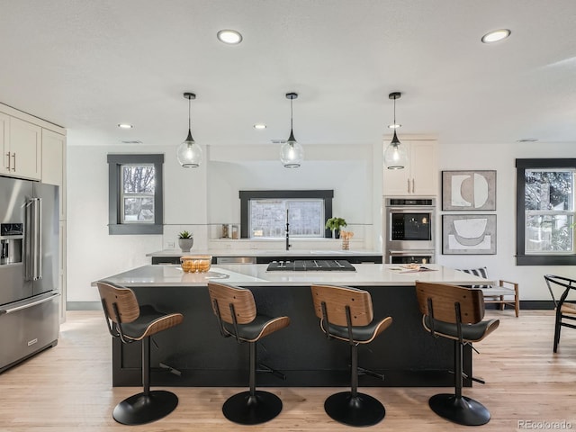 kitchen featuring pendant lighting, light countertops, appliances with stainless steel finishes, white cabinetry, and a kitchen bar