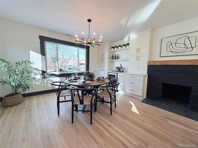 dining area featuring a brick fireplace, light wood-type flooring, visible vents, and an inviting chandelier