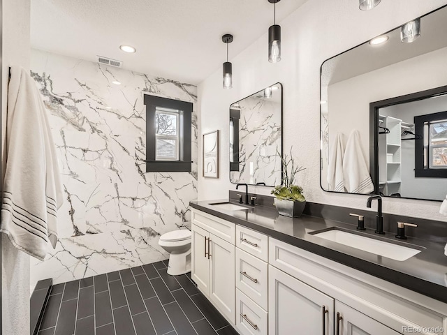 full bathroom featuring double vanity, a marble finish shower, toilet, and a sink