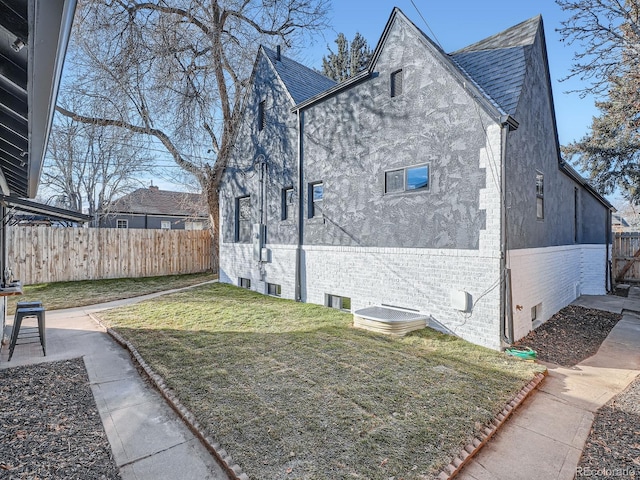 view of side of home with a lawn, roof with shingles, crawl space, fence, and brick siding