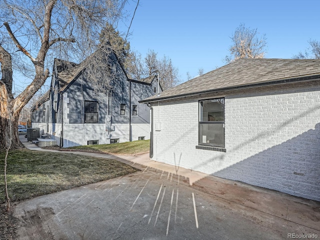 view of property exterior featuring brick siding, a lawn, and a shingled roof