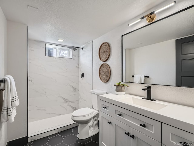 bathroom featuring toilet, a tile shower, a textured ceiling, and vanity