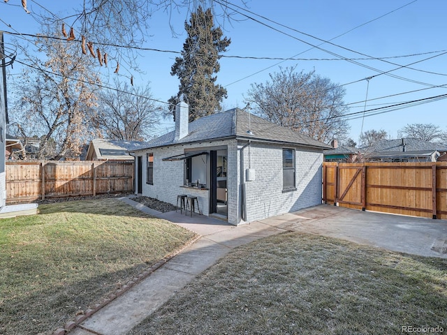 rear view of property with a lawn, a fenced backyard, a chimney, a patio area, and brick siding