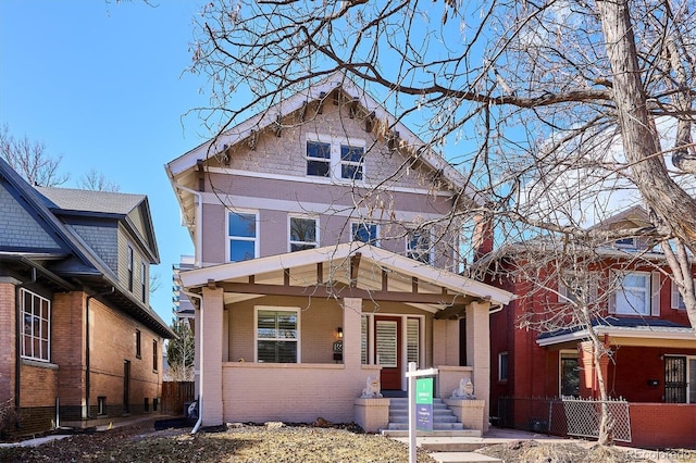 view of front of home with a porch, brick siding, and fence