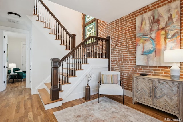 stairway with baseboards, visible vents, a towering ceiling, brick wall, and wood finished floors