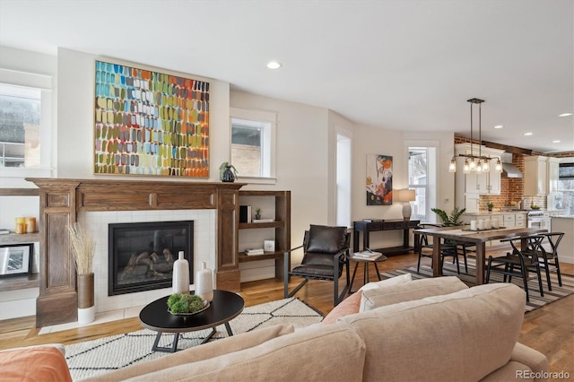 living room with a healthy amount of sunlight, a notable chandelier, a tiled fireplace, and wood finished floors