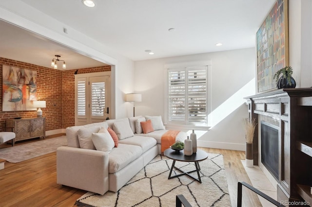 living room featuring light wood-style floors, a fireplace with flush hearth, brick wall, and a wealth of natural light