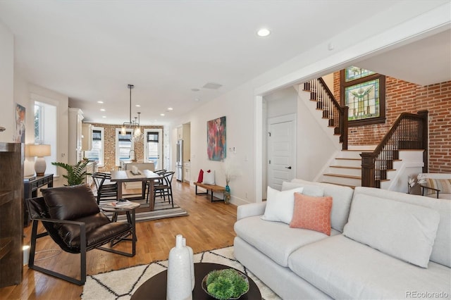 living area featuring light wood-style floors, a wealth of natural light, stairway, and brick wall