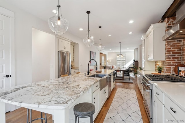 kitchen with stainless steel appliances, light wood-style floors, white cabinets, a sink, and wall chimney exhaust hood