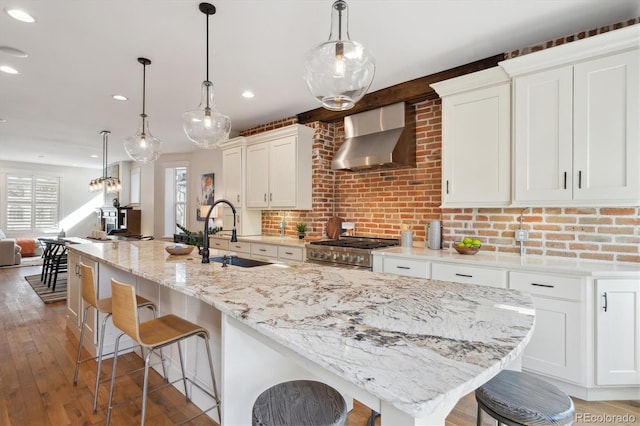 kitchen featuring wall chimney exhaust hood, a kitchen breakfast bar, high end stainless steel range, white cabinetry, and a sink