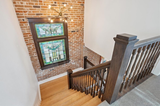 stairway featuring brick wall, wood finished floors, and baseboards