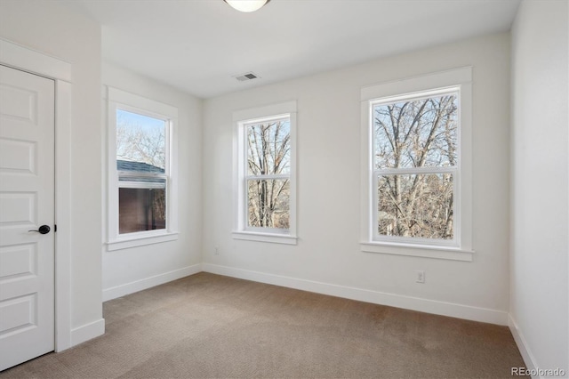 spare room with a wealth of natural light, visible vents, light carpet, and baseboards