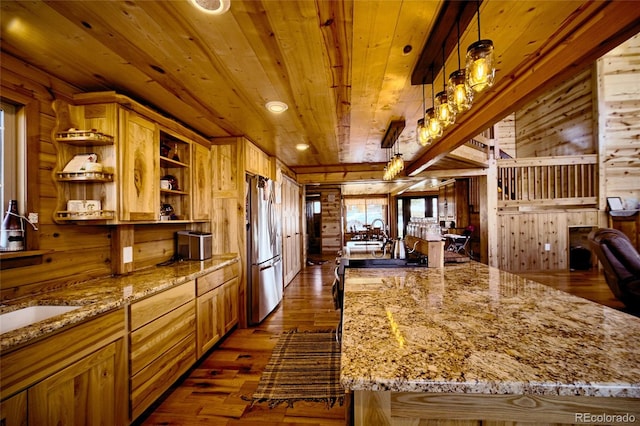 kitchen featuring light stone counters, dark wood-type flooring, pendant lighting, stainless steel refrigerator, and wood walls