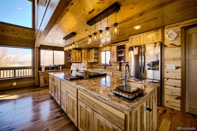 kitchen with stainless steel refrigerator, a center island with sink, dark wood-type flooring, and decorative light fixtures