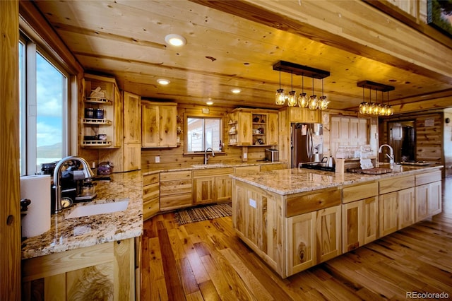 kitchen featuring a large island, light stone countertops, stainless steel fridge, decorative light fixtures, and light wood-type flooring