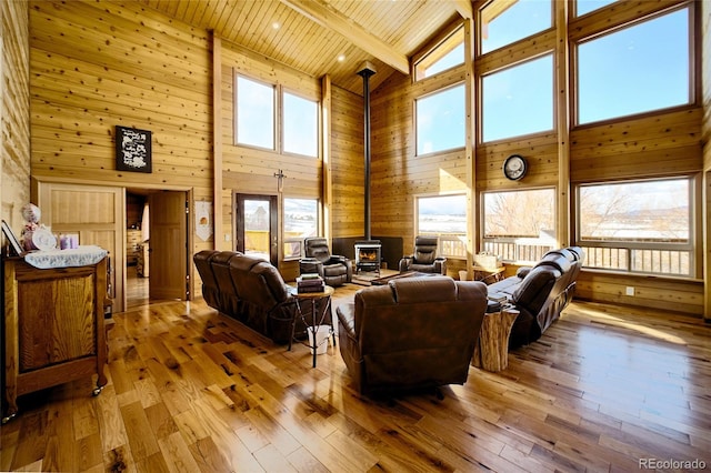 living room featuring a wood stove, hardwood / wood-style flooring, high vaulted ceiling, and wood walls