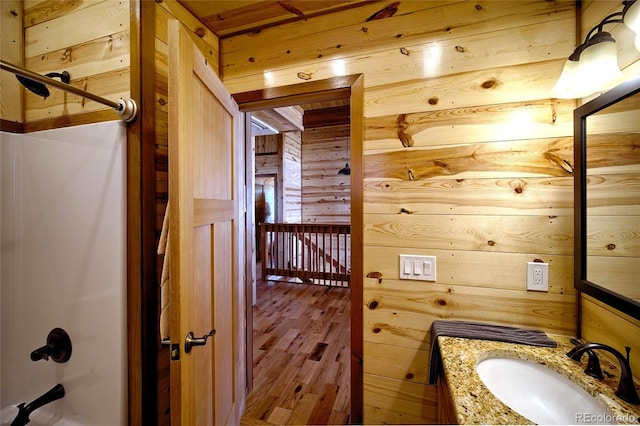 bathroom with washtub / shower combination, wood-type flooring, vanity, and wooden walls