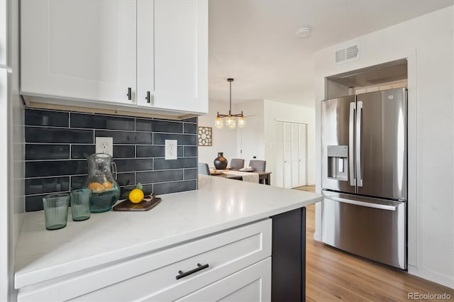 3855 S Monaco St Unit 182, Denver, CO 80237 - kitchen with stainless steel refrigerator with ice dispenser, white cabinetry, backsplash, light wood finished floors, and a chandelier