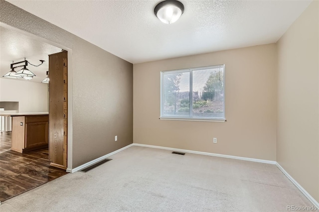 unfurnished room featuring a textured ceiling and dark carpet