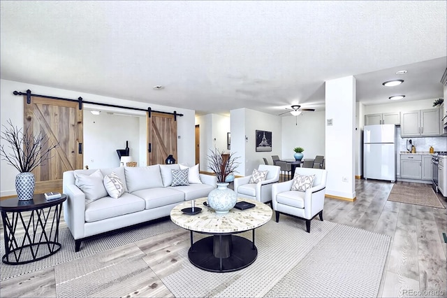 living room with light wood finished floors, a textured ceiling, a barn door, and a ceiling fan