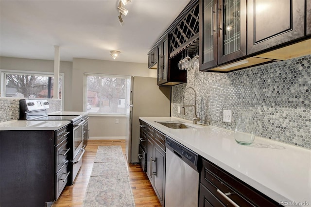 kitchen featuring decorative backsplash, dark brown cabinets, stainless steel appliances, sink, and light hardwood / wood-style floors