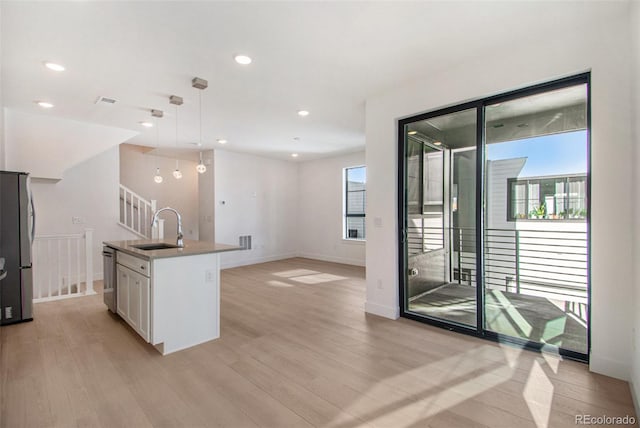 2032 S Holly St Unit 3, Denver, CO 80222 - kitchen with stainless steel appliances, white cabinetry, light wood-type flooring, hanging light fixtures, and an island with sink