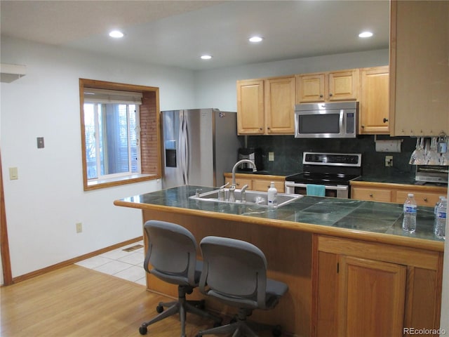 kitchen featuring a kitchen bar, sink, light hardwood / wood-style flooring, backsplash, and stainless steel appliances