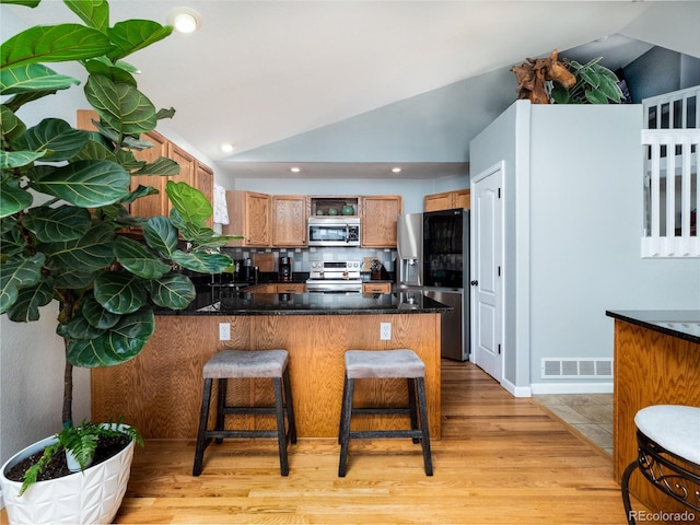 kitchen featuring lofted ceiling, tasteful backsplash, light hardwood / wood-style flooring, kitchen peninsula, and stainless steel appliances