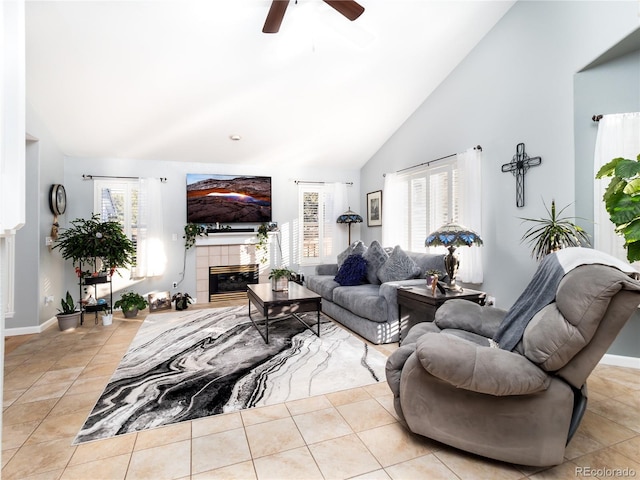 living room featuring a tiled fireplace, light tile patterned flooring, ceiling fan, and high vaulted ceiling