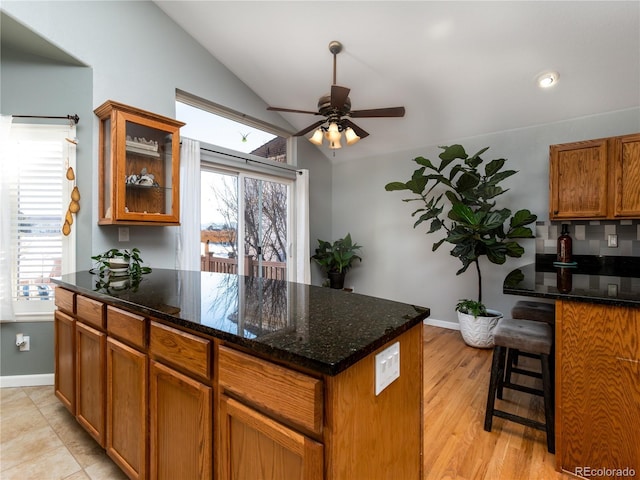 kitchen featuring a center island, vaulted ceiling, dark stone countertops, ceiling fan, and light hardwood / wood-style floors