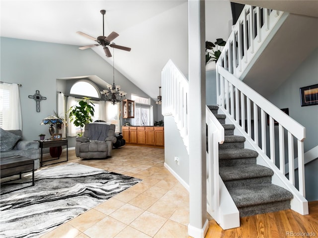 stairway with ceiling fan with notable chandelier, a wealth of natural light, tile patterned floors, and vaulted ceiling