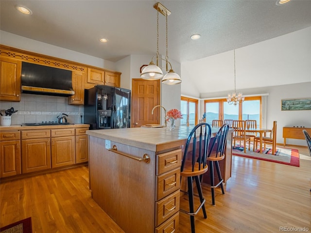 kitchen with light hardwood / wood-style flooring, hanging light fixtures, extractor fan, black appliances, and a center island with sink