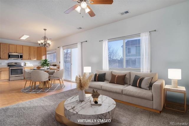 living room with ceiling fan with notable chandelier and a textured ceiling