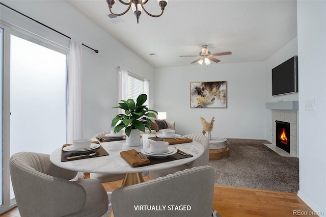 dining space featuring a fireplace, ceiling fan with notable chandelier, and light hardwood / wood-style floors