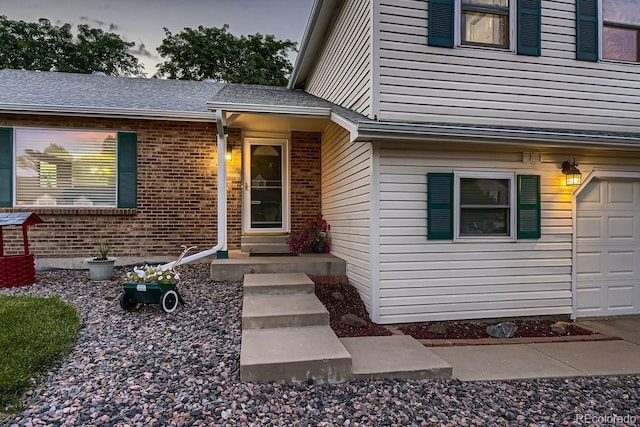 property entrance featuring a garage, roof with shingles, and brick siding